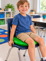 Child sitting on a green SkillSprouts OT sensory balance cushion on a blue classroom chair in a bright learning environment.