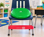 A SkillsSprouts OT therapy seat board sits on a navy blue school chair in a classroom. The therapy seat is bright green with a textured, raised surface.