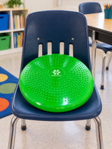 Green SkillSprouts OT sensory balance cushion positioned on a blue classroom chair in a bright learning environment.